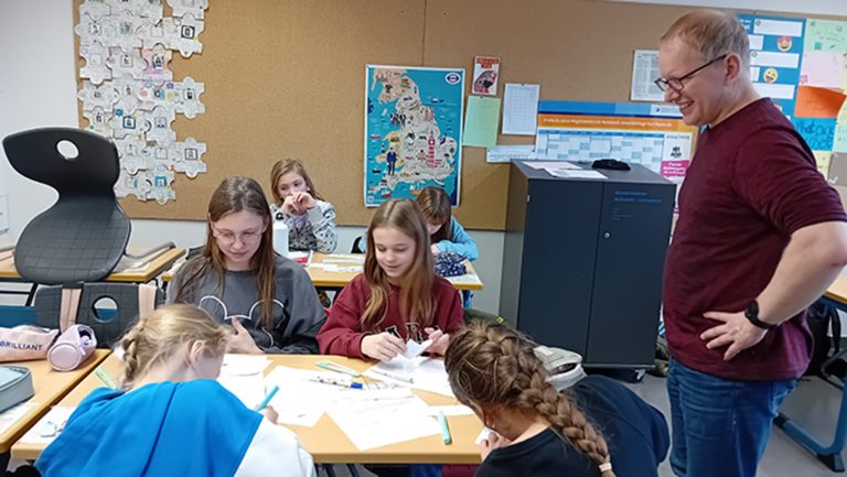 Schülerinnen mit Lehrkraft beim Erstellen von Lernplakaten