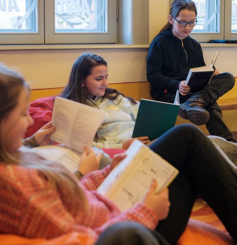 Schülerinnen und Schüler lesen in Sitzsäcken und auf Bank in Räumen der offenen Ganztagsbetreuung