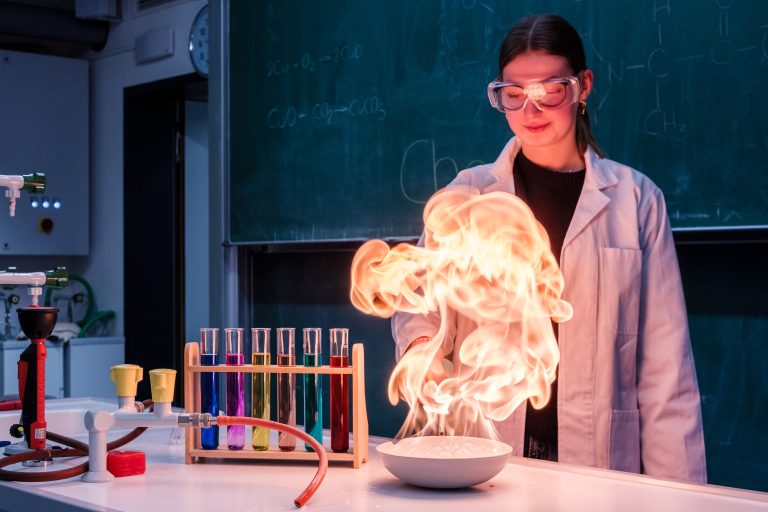 Schülerin in weißem Kittel setzt in Experiment Schüssel in Brand