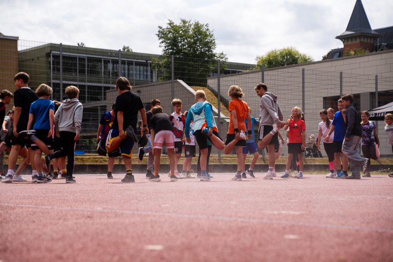 Schülerinnen und Schüler beim Aufwärmen und Dehnen auf dem Sportplatz