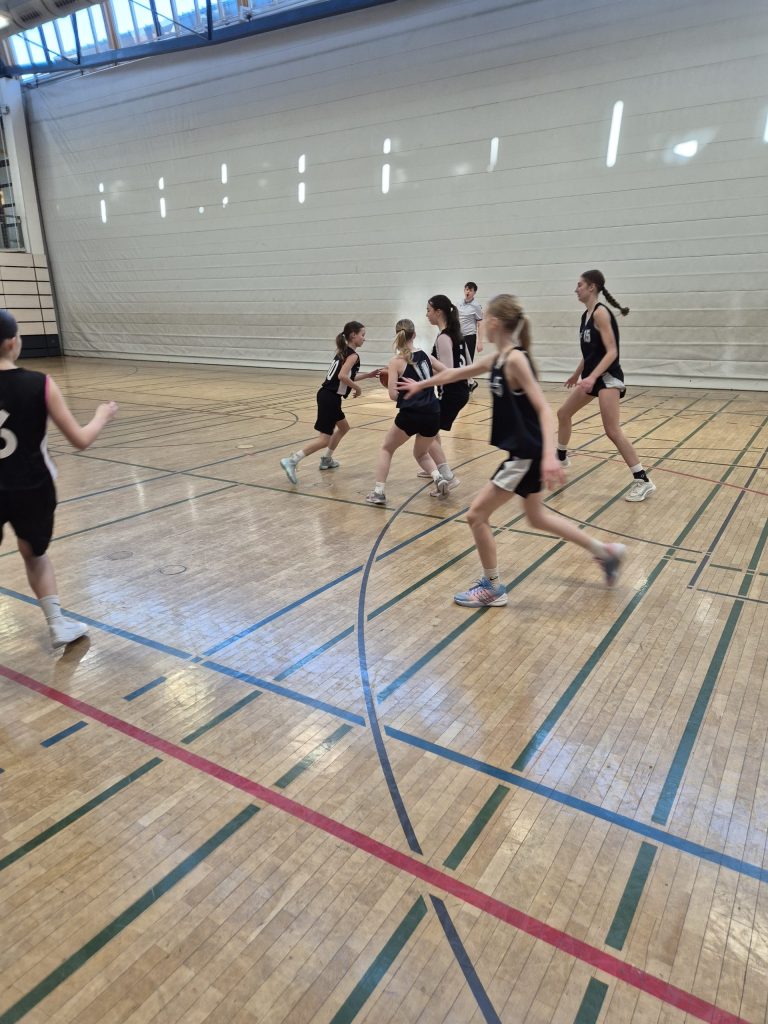 Schülerinnen in Trikots spielen Basketball in der Halle