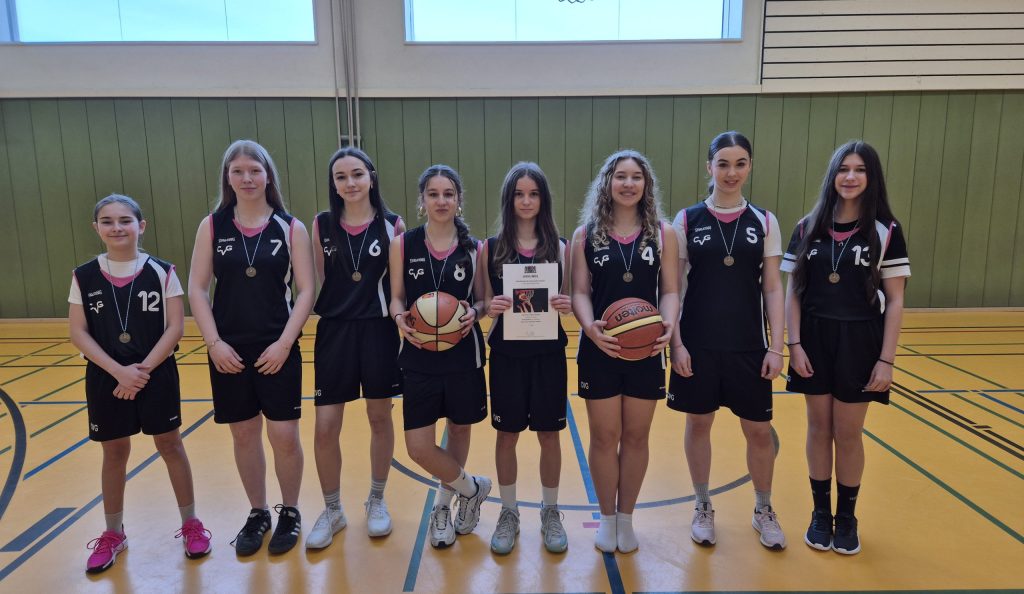 Schülerinnen in Basketball-Trikots mit Basketball und Urkunde