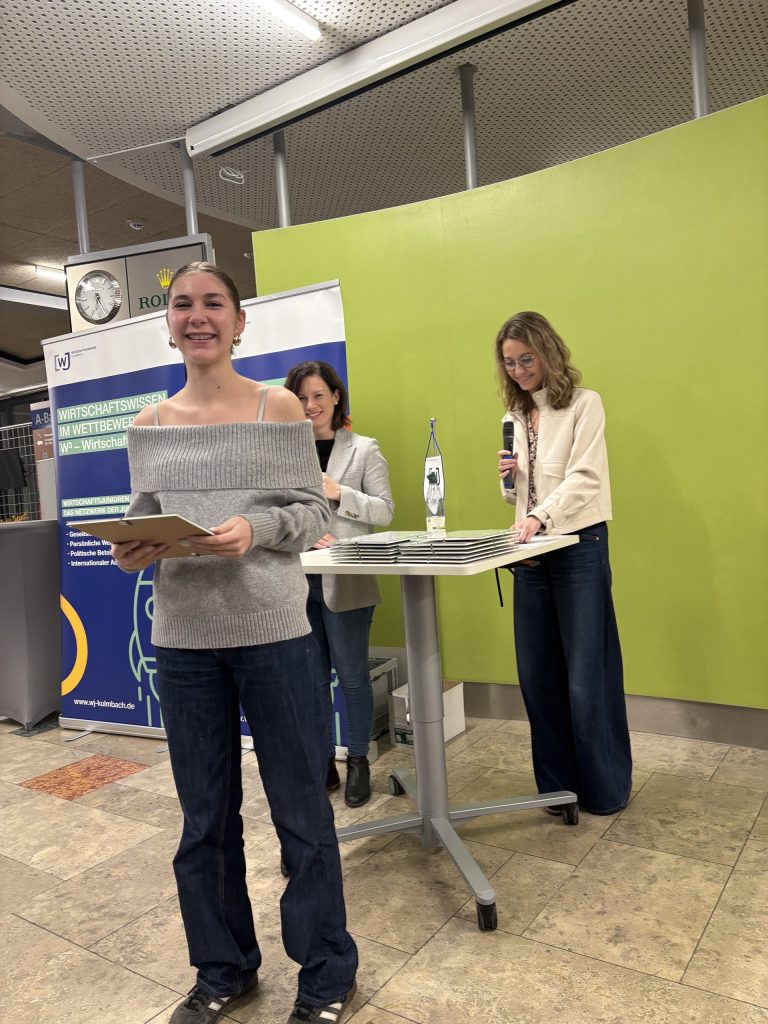 Die Preisträgerin; Schülerin lächelt und hält gerahmte Urkunde