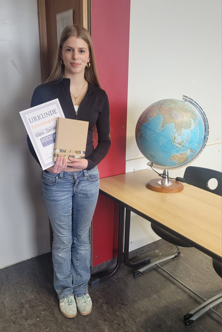 Schülerin steht neben Globus in Klassenzimmer und hält Preis und Urkunde des Diercke-Wettbewerbs in der Hand