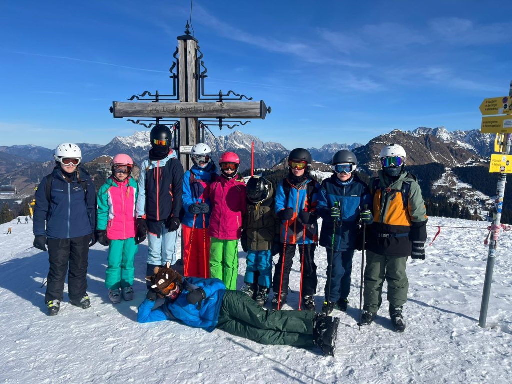 Schülerinnen und Schüler in Skikleidung vor Gipfelkreuz auf schneebedecktem Berg