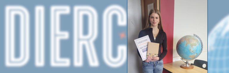 Schülerin steht neben Globus in Klassenzimmer und hält Preis und Urkunde des Diercke-Wettbewerbs in der Hand; im Hintergrund das Diercke-Wissen-Logo