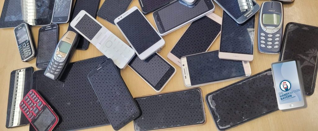 Gesammelte alte Handys auf einer Tischplatte; Logo der Handyaktion Bayern unten rechts