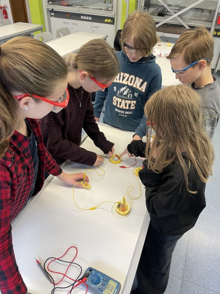 Schülerinnen und Schüler mit Schutzbrillen an einem Tisch mit Versuchsaufbau
