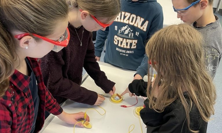 Schülerinnen und Schüler mit Schutzbrillen an einem Tisch mit Versuchsaufbau