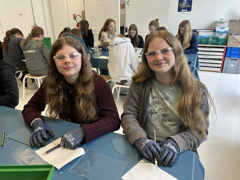 Schülerinnen mit Schutzbrillen basteln ein Haus aus Glas