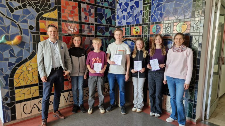 Schülerinnen und Schüler präsentieren ihre Urkunden. Links der Schuleiter, rechts die Mathematiklehrkraft