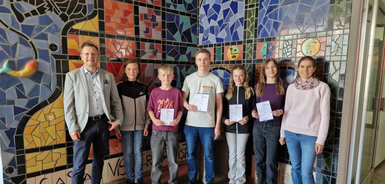 Schülerinnen und Schüler präsentieren ihre Urkunden. Links der Schuleiter, rechts die Mathematiklehrkraft