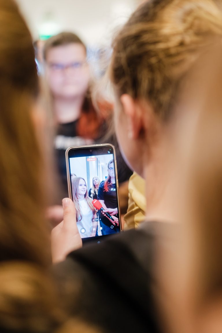 Schülerin wird von TVO interviewt; andere Schülerin filmt mit Handy