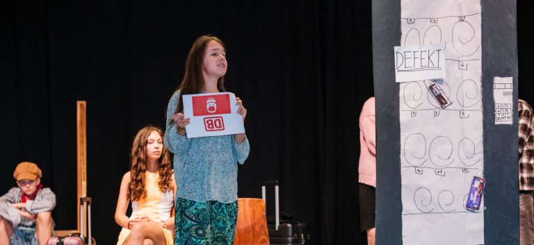 Schülerin steht auf der Bühne und hält Schild vor sich