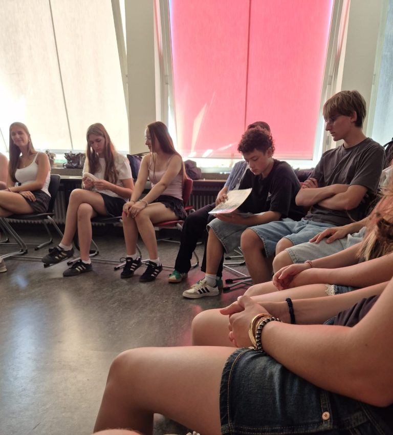 Schülerinnen und Schüler sitzen im Kreis und führen Gespräch mit Gast