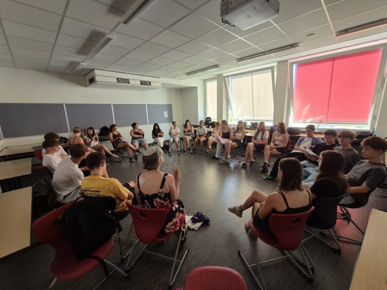 Schülerinnen und Schüler sitzen im Kreis und führen Gespräch mit Gast