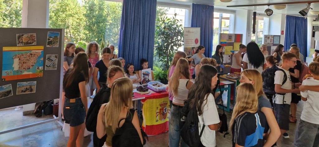 Schülerinnen und Schüler verkaufen Kuchen in der Pausenhalle. Die Tische sind mit spanischen Flaggen dekoriert.