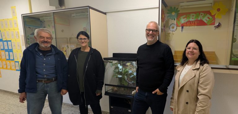 Biologielehrkraft mit Vertretern und Vertreterinnen des Elternbeirats neben dem gespendeten Terrarium